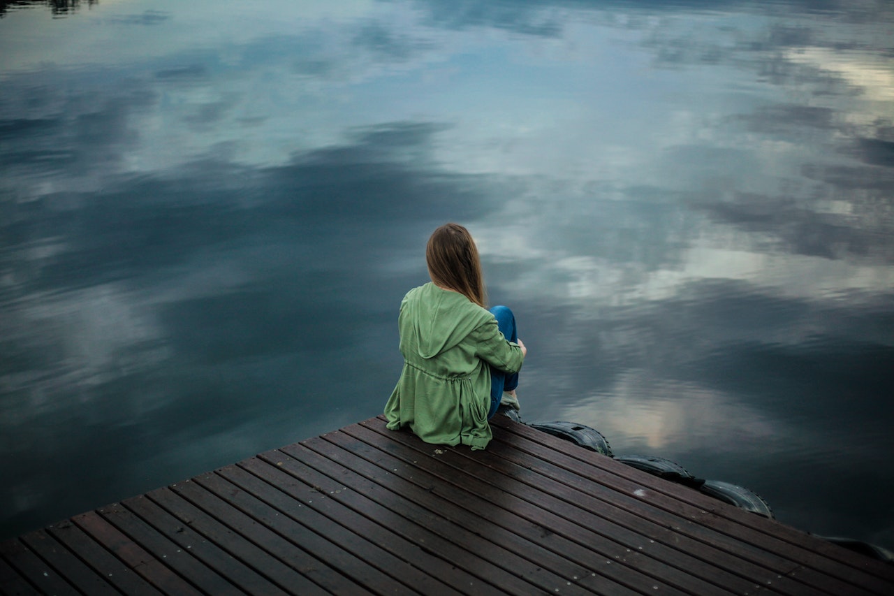 Woman sitting across a lake thinking